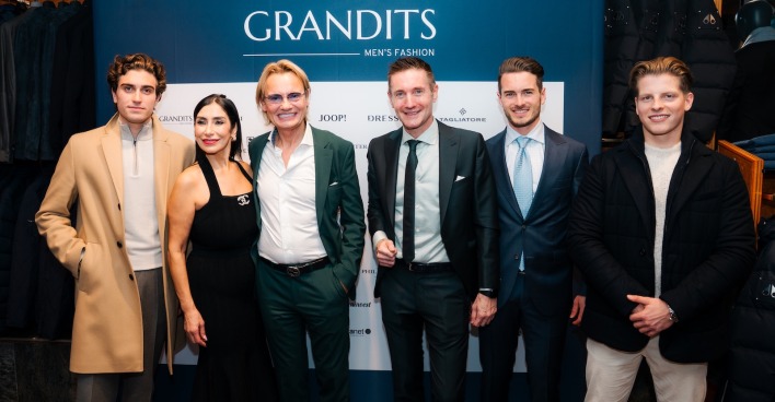 Sechs Männer und eine Dame vor einer türkisen Wand im  Grandits Men's Fashion-Store