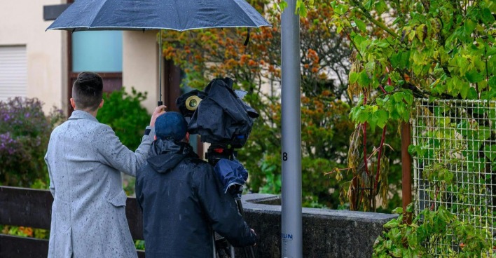 Journalistenteam mit Kamera und Regenschirm dokumentiert den Tatort in Enns nach dem mutmaßlichen Doppelmord.