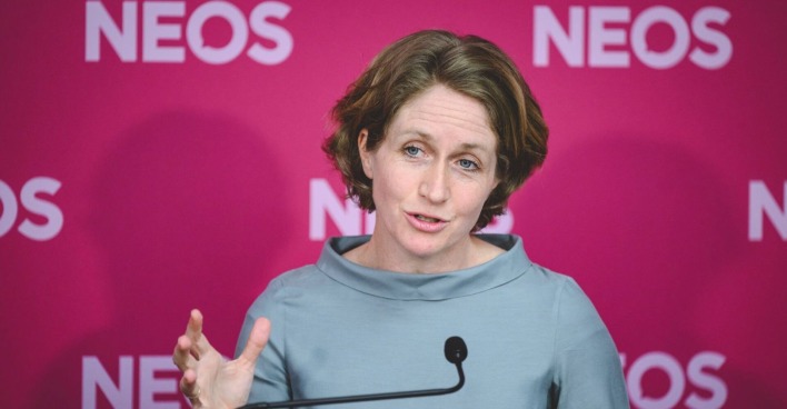 Stephanie Krisper steht vor einem pinken NEOS-Hintergrund und spricht bei einer Pressekonferenz, während sie eine Handgeste macht. Jetzt hat sie ihr Mandat zurückgelegt.