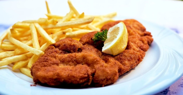 Teller mit Wiener Schnitzel, Zitronenspalte und Pommes frites, traditionelles österreichisches Gericht wie es auch  im Thomawirt serviert wird.