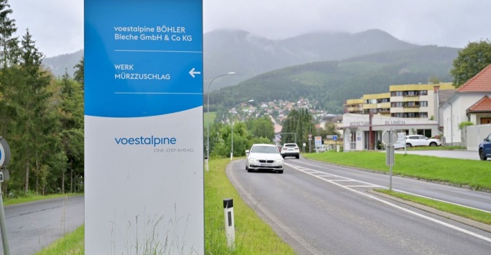 Einfahrtsschild des Voestalpine-Werks Böhler Bleche in Mürzzuschlag mit Blick auf die Straße und die umliegende Stadt im Hintergrund.