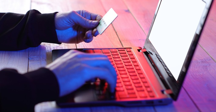 Person vor einem rot beleuchtenden Laptop mit einer Kreditkarte