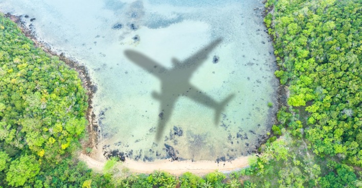 Luftaufnahme einer Küste mit grünem Wald und türkisfarbenem Wasser, in dem der Schatten eines Flugzeugs zu sehen ist. Symbolfoto für die Einstellung des Flugbetriebs der Regionalfluglinie Blue Islands.