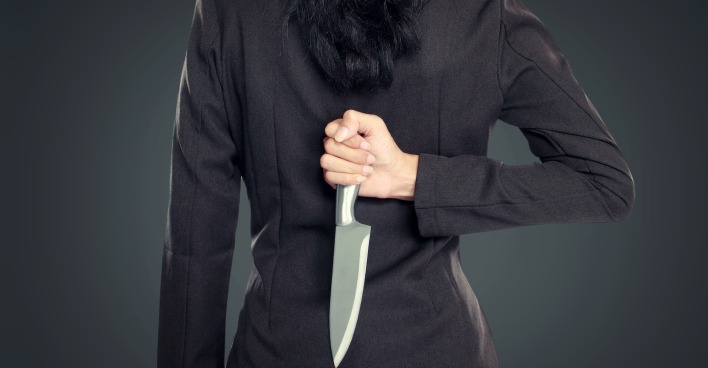 Frau in Kostümjacke von hinten mit Messer in der Hand