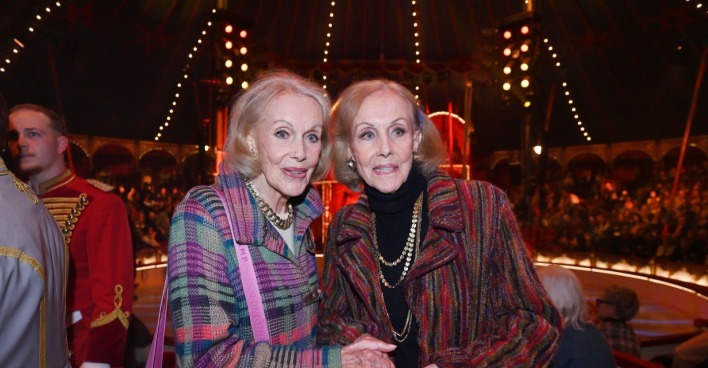 Alice und Ellen Kessler stehen eng nebeneinander im Zuschauerbereich des Circus Roncalli; die Kessler-Zwillinge lächeln in die Kamera während ihres letzten öffentlichen Auftritts.