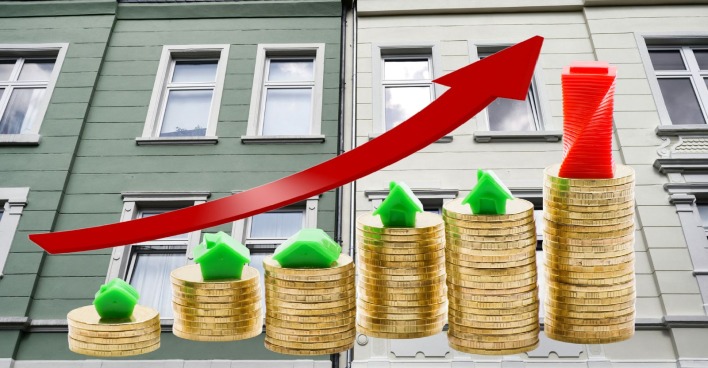 Symbolbild steigende Mietpreise: Münzstapel mit Häusern und rotem Aufwärtspfeil vor Wohnhausfassaden als Darstellung der Mietkostenentwicklung 2025 in Österreich.