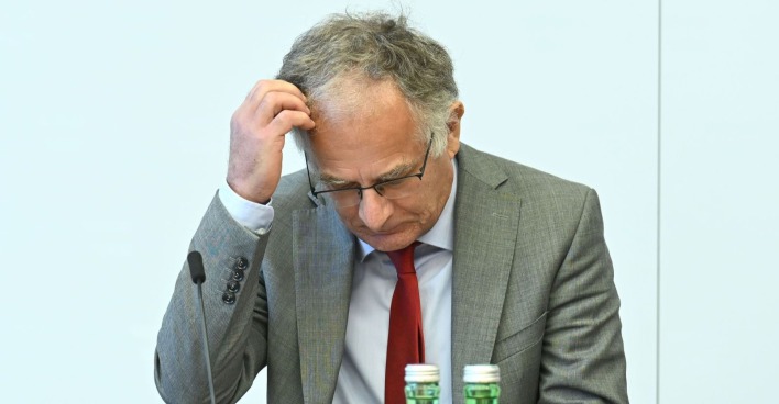 Finanzminister Marterbauer im grauen Anzug und roter Krawatte blickt nachdenklich nach unten, während er sich an den Kopf fasst – Symbolbild zur Budgetkrise in Österreich.