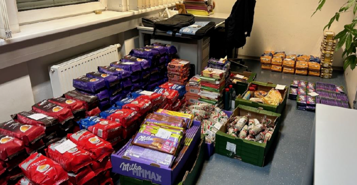 Mehrere Stapel von beschlagnahmten Lebensmitteln, darunter Kaffeepackungen, Milka-Schokolade und Wurstwaren, auf dem Boden eines Polizeibüros.