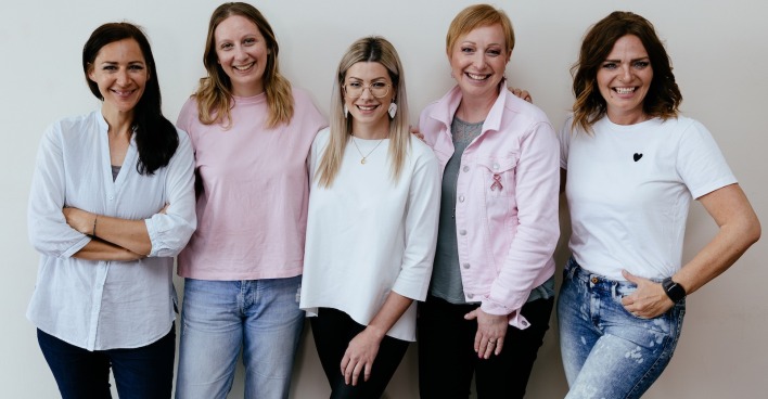 Fünf Frauen in Shirts, Pullovern und Jacken vor einer weißen Wand