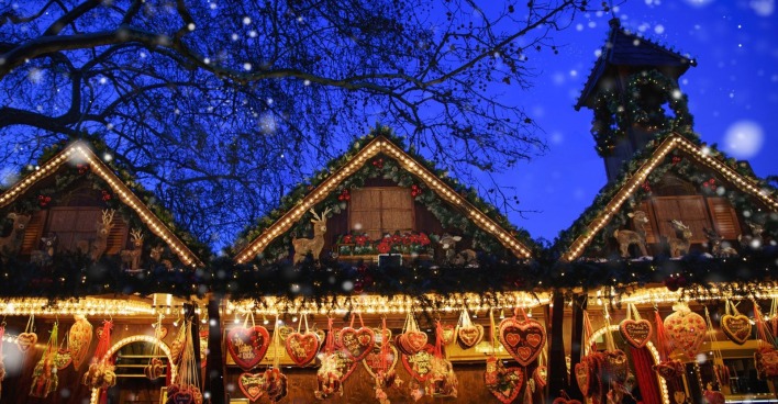 Beleuchtete Weihnachtsmarktstände mit Lebkuchenherzen und Weihnachtsdekoration am Abend, Symbolbild für die Diskussion um Bargeld- und Kartenzahlung auf Märkten.