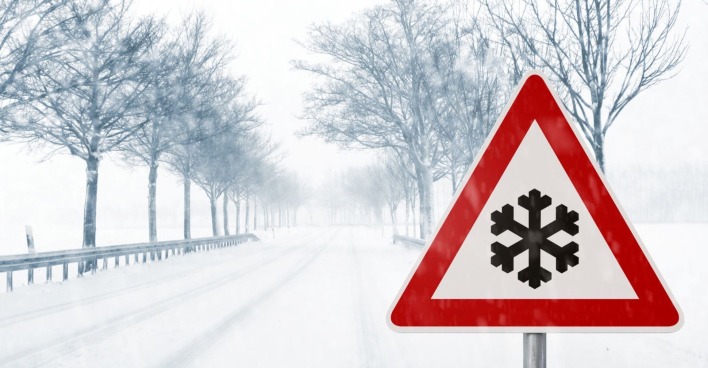 Warnschild mit Symbol für starken Schneefall auf einer verschneiten Landstraße
