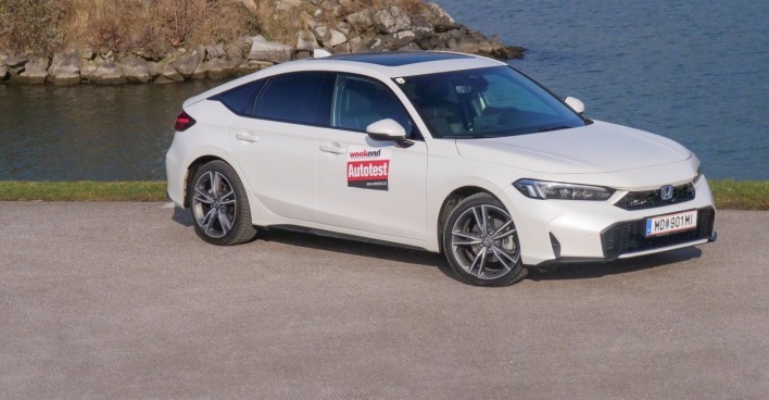 Ein weißer Honda Civic parkt am Ufer eines Gewässers.. Das Auto das auf einem betonierten Parkplatz steht leuchtet in der Sonne.