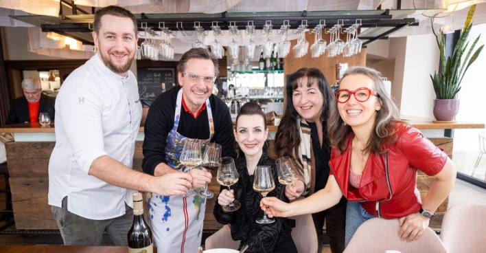 Zwei Männer und drei Frauen stoßen mit einem Glas Wein an