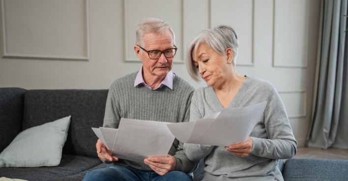 Älteres Paar prüft zu Hause gemeinsam Unterlagen zur Pension und privaten Altersvorsorge.