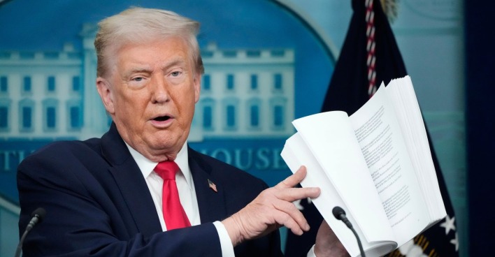 Donald Trump hält ein aufgeschlagenes Dokument in den Händen und erklärt die Inhalte seines geplanten internationalen Friedensrats im Weißen Haus.