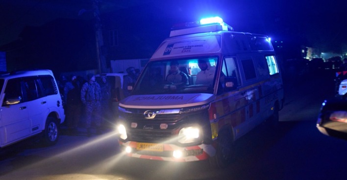 Ambulanzfahrzeug mit eingeschaltetem Blaulicht in einer dunklen Straße in Amritsar, umgeben von Einsatzkräften und Fahrzeugen.