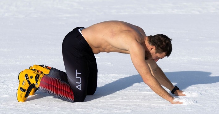 Benjamin Karl kniet nach dem Olympiasieg im Snowboard Parallel-Riesentorlauf in Livigno im Schnee, oben ohne nach seinem Jubel im Zielraum bei Olympia 2026.