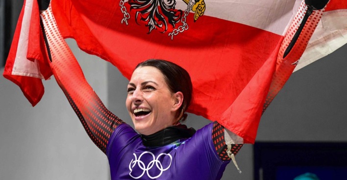 Janine Flock feiert in Cortina d’Ampezzo ihren Olympia-Sieg im Skeleton und hält die österreichische Fahne über sich.