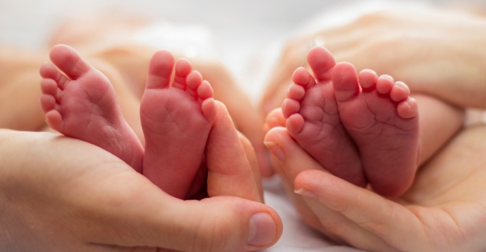 Zwillinge: Mutter und des Vaters Hände wiegt zwei Babys Füße auf einem blassen Hintergrund