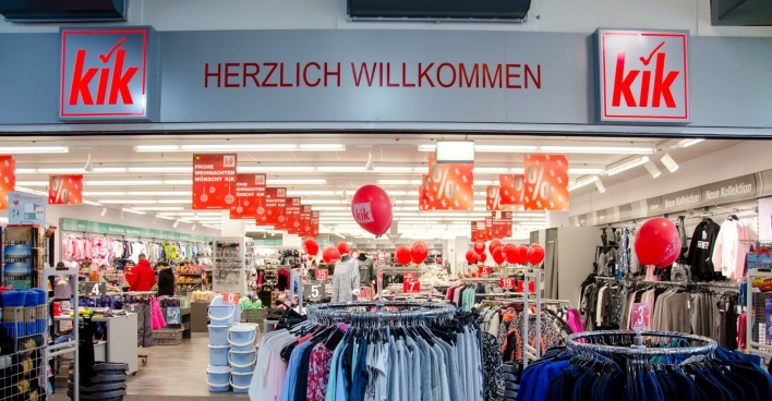 Innenansicht einer KiK-Filiale mit Kleiderständern, roten Rabatt-Schildern und KiK-Logo über dem Eingang – Kik schließt auch in Österreich Filialen