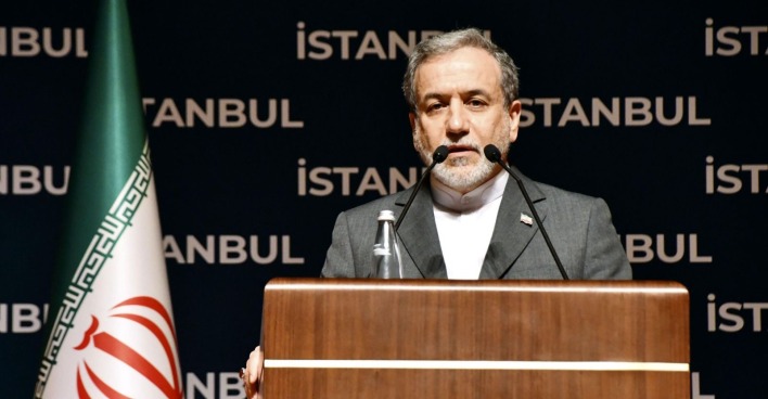 Iranischer Politiker steht am Rednerpult mit iranischer Flagge im Hintergrund während einer Veranstaltung in Istanbul.