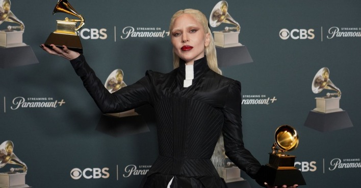 Eine blonde Frau im schwarzen Kleid hält zwei Trophäen hoch