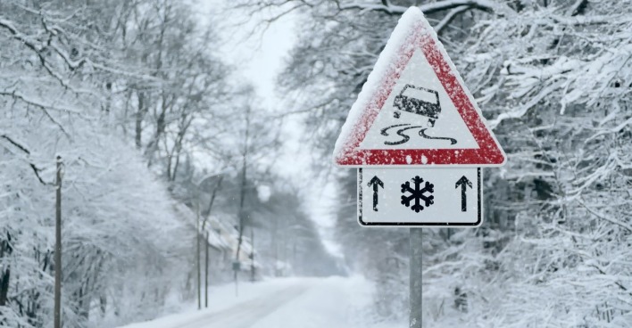 Verschneite Straße mit Warnschildern von Rutschgefahr für Autos.