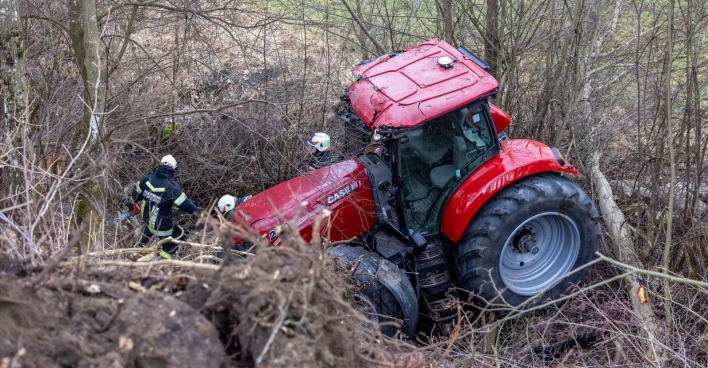 Ein roter Traktor hängt im Gebüsch, rundherum sind Feuerwehrleute