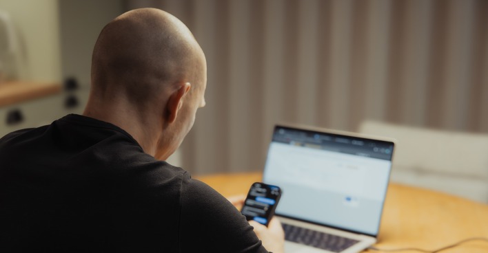 Mann hinter dem Laptop mit Smartphone in der Hand | Credit: TimelessNordic/Shutterstock