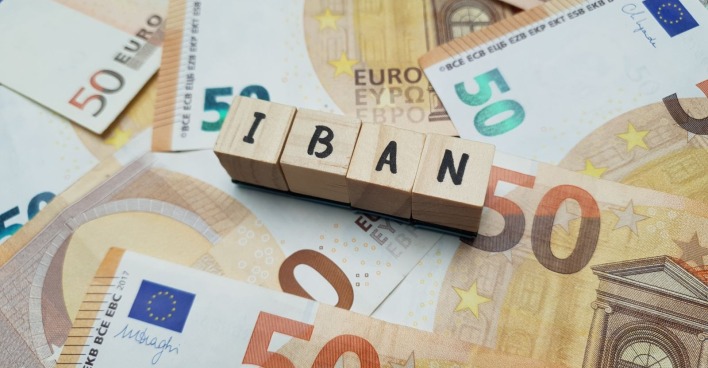 50 Euro-Banknoten hinter Holzklötzen auf denen das Wort "IBAN" geschrieben steht