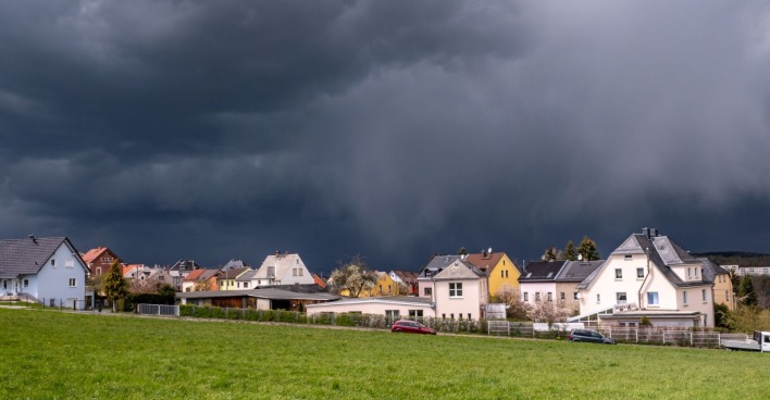 Gewitter am Ostersonntag: Dunkle Gewitterwolken über einem österreichischen Dorf mit Blick über eine saftig grüne Wiese im Frühling
