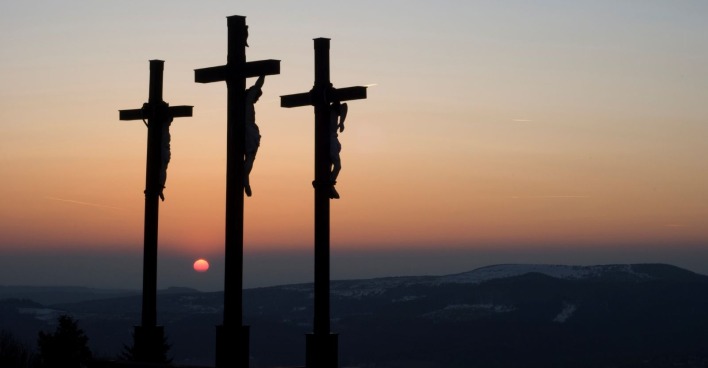 Kreuzigung Jesu auf Golgotha mit drei Kreuzen bei Sonnenuntergang; Themenbild für Karfreitag Bedeutung, Rituale und Traditionen.