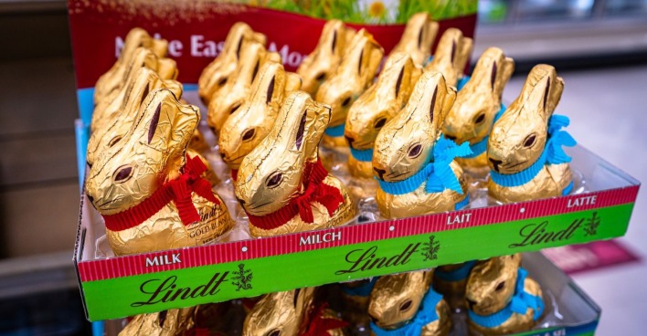 Mehrere Lindt Goldhasen stehen dicht nebeneinander in einem Supermarktregal und zeigen die typische goldene Verpackung mit Schleife.