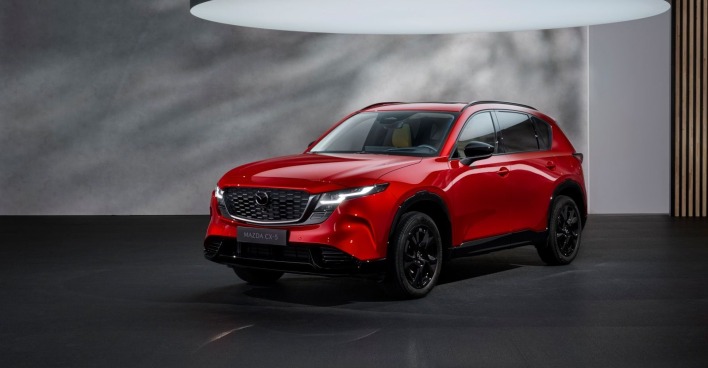 Eine roter Mazda CX 5 steht einem grau-schwarzen Raum. Über dem Auto ist ein sehr großes Licht zu sehen, das das Auto beleuchtet.