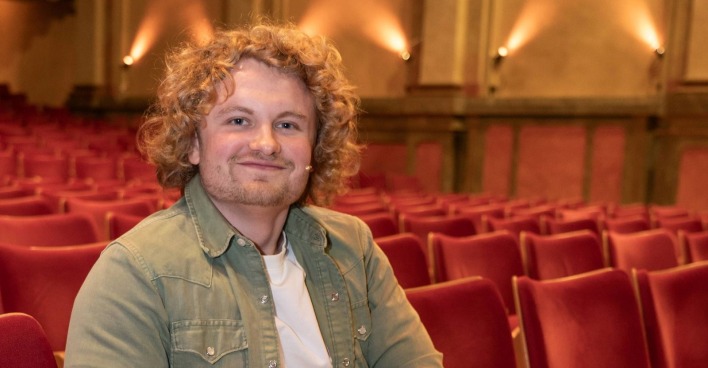 Dr. Bohl sitzt im Zuschauerraum eines Theaters in Wien und präsentiert seinen außergewöhnlichen ESC-Song „Schnitzel (all night long)” für den Eurovision Song Contest 2026.