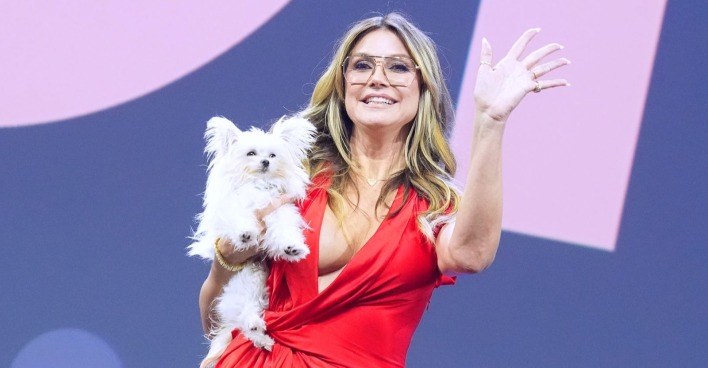 Eine blonde Frau in rotem Kleid hält einen weißen Hund auf dem Arm