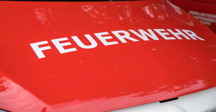 Nahaufnahme einer roten Feuerwehrlasterhaube mit 'FEUERWEHR'-Text, die das Design von Notfallfahrzeugen und die städtische Umgebung hervorhebt.