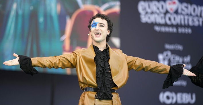 Ein Mann mit blauem Stern im Gesicht streckt die Arme aus