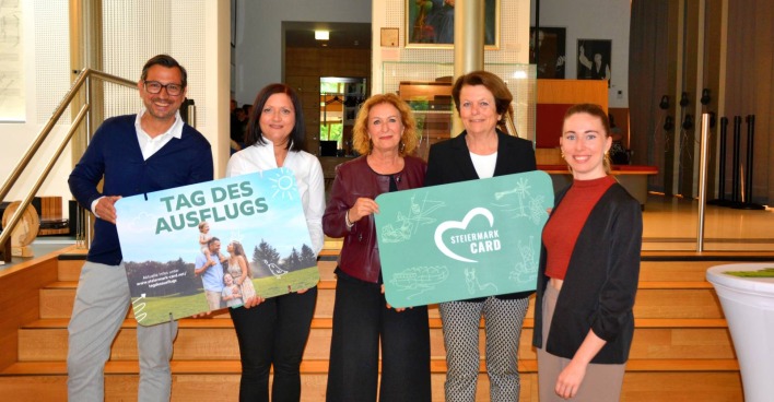 Jörg Ehtreiber (KIMUS Kindermuseum Graz GmbH), Anita Klug (GF Steiermark-Card), Doris Wolkner-Steinberger (Gesellschafterin Steiermark-Card), Elisabeth Weixler (Gesellschafterin Steiermark-Card), Maria Lackner (Salon Stolz) halten vor einer Treppe im Salon Stolz große Modelle der Steiermark-Card in Händen