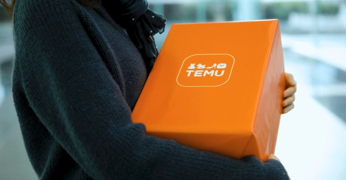 Eine Person im dunkelblauen Pullover trägt ein oranges Temu-Paket