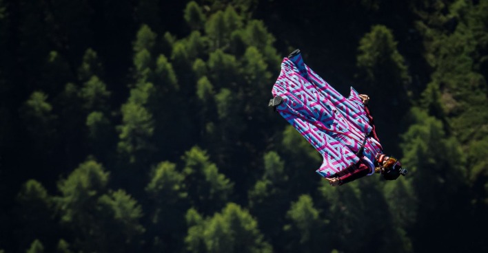 Frau fliegt in einem Wingsuit über einen Wald