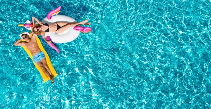 Junges Pärchen auf Luftmatratzen im Pool | Credit: New Africa/Shutterstock