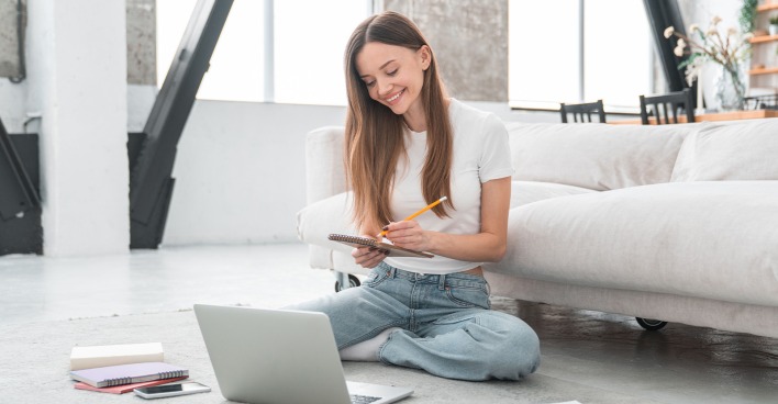 Frau sitzt am Boden ihres Eigenheims und macht sich Notizen vor ihrem Laptop | Credit: Inside Creative House/Shutterstock