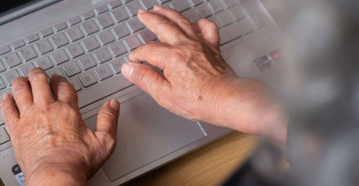 Ältere Arbeitnehmerin tippt auf einem Laptop – das neue Sparpaket bringt höhere Abgaben und Änderungen bei der Arbeitslosenversicherung ab 2027.