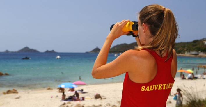 Bademeisterin in rotem Shirt sieht aufs Meer mit einem Fernglas
