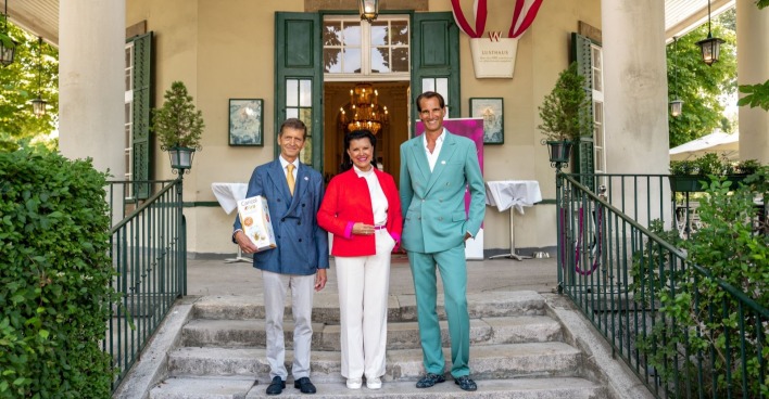 Zwei Männer im Anzug und eine Dame in weißer Hose und Bluse sowie roter Jacke auf den Stufen des Wiener Lusthauses