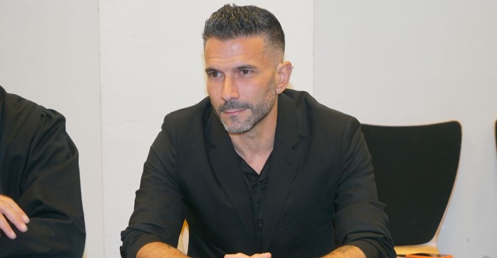 Marc Terenzi sitzt bei einer Veranstaltung in einem schwarzen Anzug an einem Tisch und blickt konzentriert nach vorne.