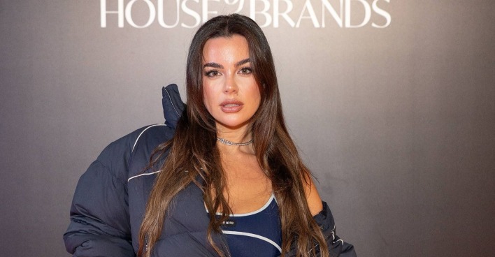 Nadine Mirada bei einem Fashion-Event in dunklem Outfit und Oversize-Jacke. Das österreichische Curvy-Model posiert vor einer Fotowand und blickt selbstbewusst in die Kamera.