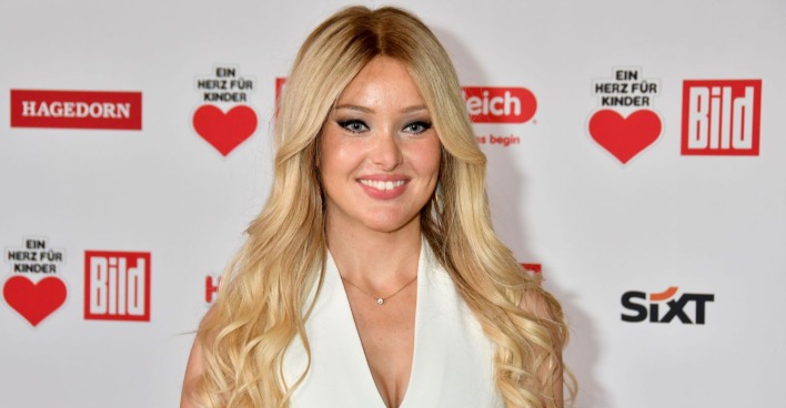 Blonde Frau in weißem Kleid lächelt in die Kamera