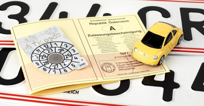Zulassungsschein, ein Pickerl sowie ein Miniaturauto sind zu sehen